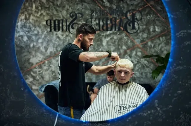 Barber strihá blonďavého zákazníka pred okrúhlym zrkadlom
